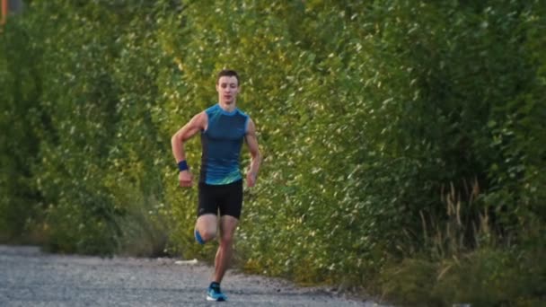 Hombre fuerte corredor muscular corriendo en el parque al atardecer, cámara lenta, gran ángulo — Vídeo de stock