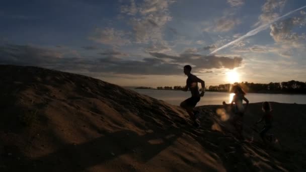 Група спортсменів - двоє дівчат і хлопець тікають з гори, біля річки в сутінках, повільний рух — стокове відео