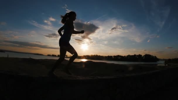 Бегущая молодая женщина в парке на закате, замедленная съемка, руки в кулаке, силуэт — стоковое видео