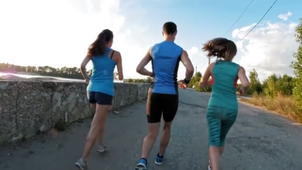 Un grupo de atletas - dos chicas y un tipo corriendo en el parque de la ciudad, cerca del río, en cámara lenta — Vídeo de stock
