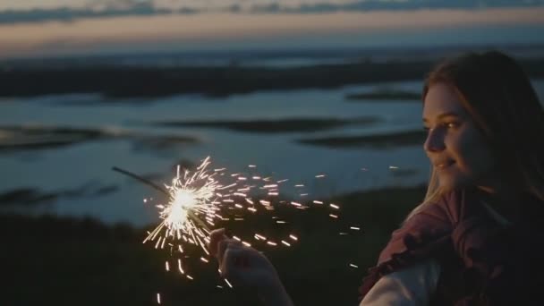 Mulher bonita está em uma colina alta com sparkler ao pôr do sol em câmera lenta — Vídeo de Stock