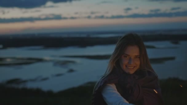 Smiling young woman stands on a high hill with sparkler at sunset in slow motion — Stock Video