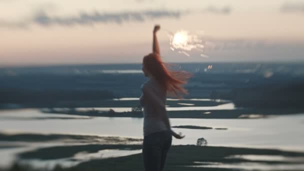 Mujer joven sonriente bailando en una colina alta con chispa al atardecer — Vídeo de stock