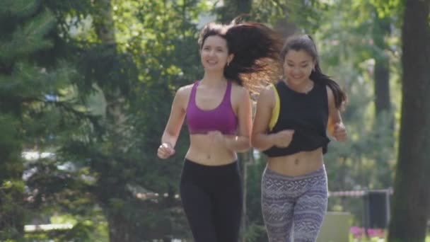 Två attraktiva Fitness athletic unga kvinnor med lockigt hår kör i parken på sommarmorgon, slow motion — Stockvideo