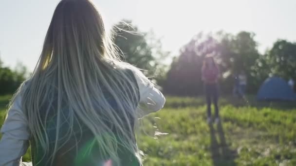 Mujer joven en pantalones vaqueros azules y zapatillas blancas lanzando un frisbee en el día de verano en el prado en la colina alta hacia el sol, cámara lenta — Vídeos de Stock