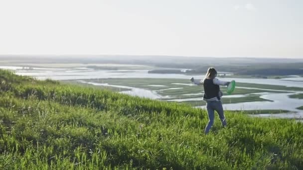 Jeune femme attirante jetant un frisbee à la journée d'été sur la prairie en haute colline, au ralenti — Video
