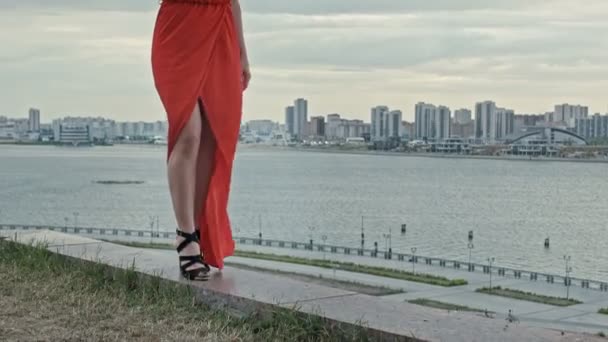 Ноги молодой женщины в красном платье, идущей по ветру с развевающимся платьем — стоковое видео