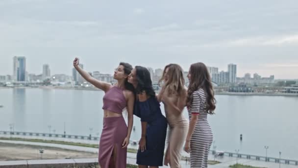 Cuatro atractivas mujeres jóvenes en vestidos de fiesta en la colina alta obtener un selfie, tiro ancho — Vídeo de stock