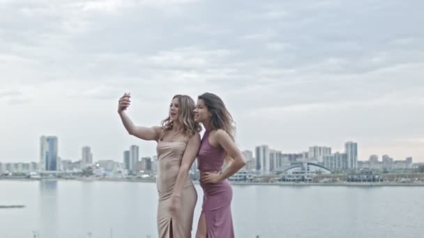 Duas mulheres jovens atraentes em vestidos de festa em alta colina obter uma selfie por smartphone, tiro largo — Vídeo de Stock