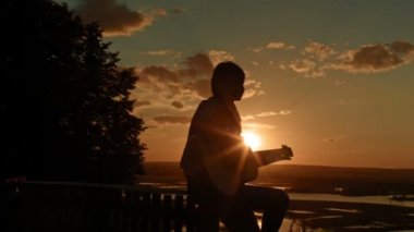 Akustik gitar çalmak genç romantik kadın yüksek tepede kamp yakınındaki batımında, siluet