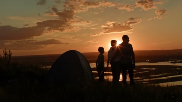 La jeune famille - père, mère et fils dans le camping - se tient sur une haute colline au coucher du soleil d'été, à la recherche de paysage, de silhouette — Video