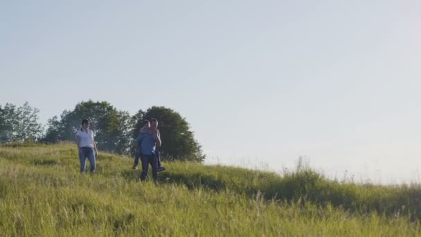 Família feliz em férias de verão - pai, mãe e filho à noite. se divertindo e andando ao longo da colina alta — Vídeo de Stock