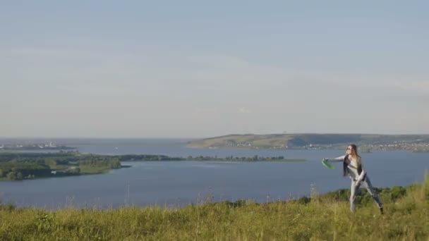 Une jeune fille lance un frisbee vert à la journée d'été sur la haute colline — Video