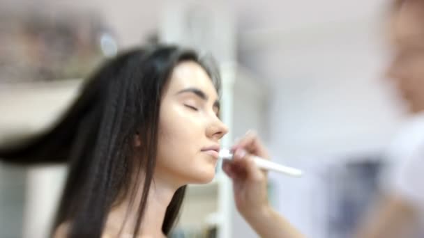 Maquillaje artista hace para chica atractiva hermoso maquillaje, peluquero hace peinado: trabajo para el cabello — Vídeo de stock