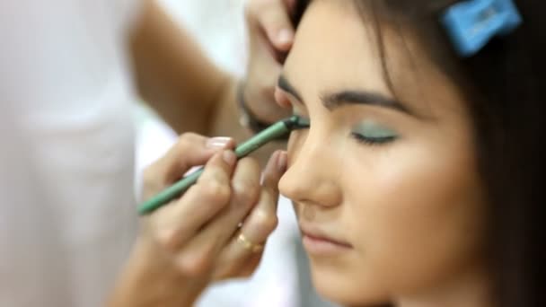 Maquillaje artista hace para chica atractiva hermoso maquillaje, peluquero hace peinado: trabajo para los ojos, primer plano — Vídeo de stock