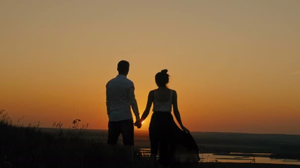 Couple aimant jeune homme courageux et belle fille se tient sur la haute colline et regardant à la silhouette coucher de soleil, slider shot — Video