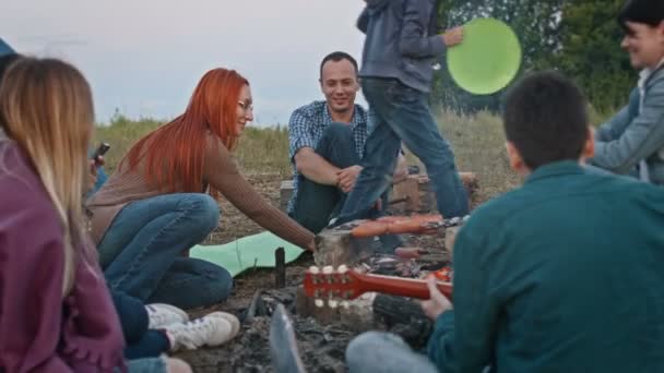 Amigos felices cocinando barbacoa cerca de fogata y toca la guitarra al aire libre — Vídeo de stock