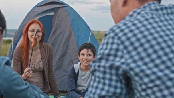 Glada vänner matlagning bbq nära lägerelden och spelar gitarr utomhus, äta wieners, camping på hög kulle — Stockvideo