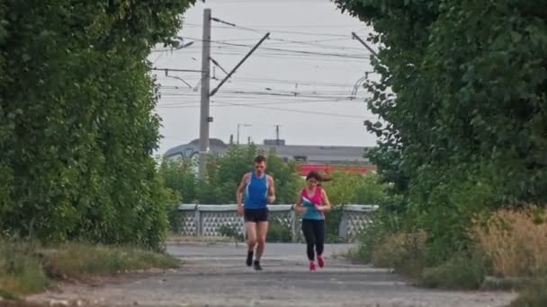 Біг спортивна пара бігунів тренування в парку, над поїздом — стокове відео