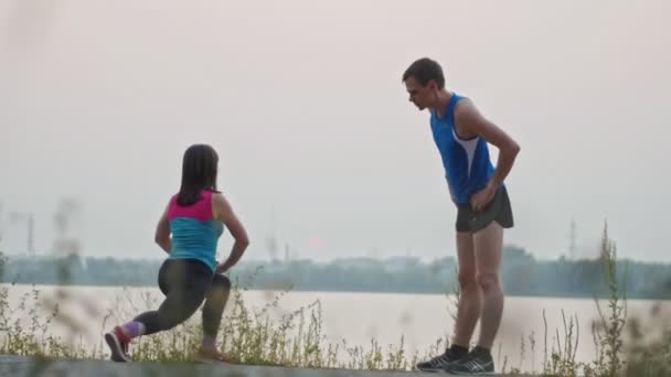 Par stretching tillsammans i parken i skymningen, över floden — Stockvideo
