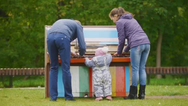 Família feliz: Pai, Mãe e criança - menina caminhando no parque de outono: tocando perto do piano — Vídeo de Stock