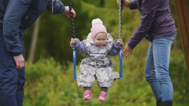 Jovem família feliz no parque infantil - pai, mãe e filha bebê rindo - balanço das crianças, câmera lenta — Vídeo de Stock