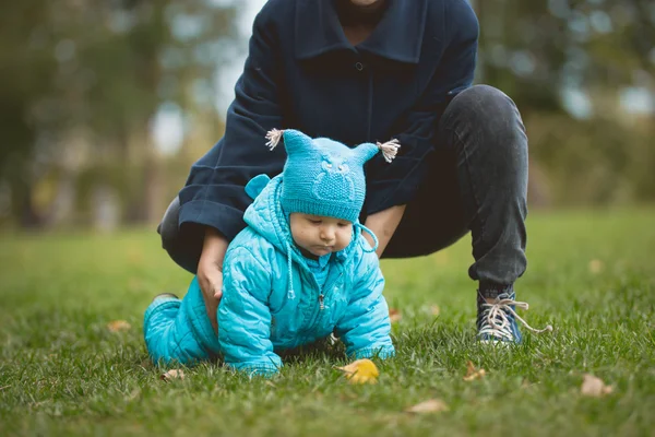 Familia feliz caminando en el parque de otoño: niño arrastrándose sobre la hierba con la madre — Foto de Stock