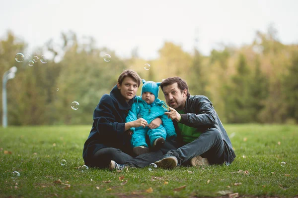 Familia caminando en el parque de otoño - Padre, madre e hijo pequeño sentados en el prado —  Fotos de Stock