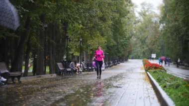Runner genç kadın sonbahar park açık havada egzersiz yağmur, pembe eğitim takım elbise, ağır çekim çalıştırmak için