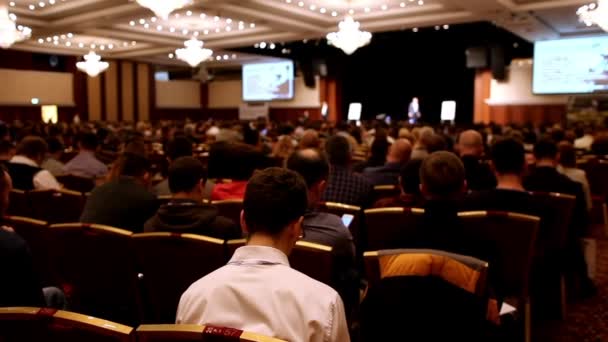 Conferenciante cuenta y muestra la presentación en la escena a la casa llena de oyentes — Vídeo de stock