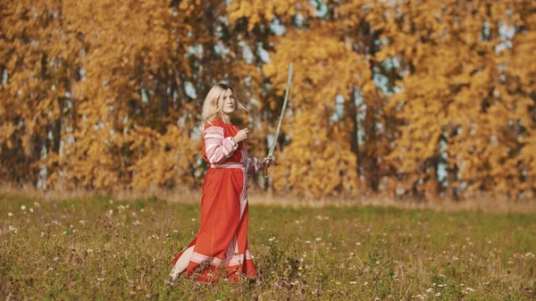 Militan kadın elinde kılıçla sonbahar tarlasında koşuyor. — Stok fotoğraf
