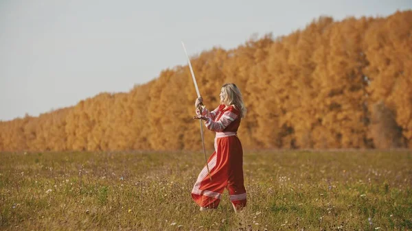 Militante donna in abito rosso che allena il suo gioco di spada sul campo di autunno — Foto Stock