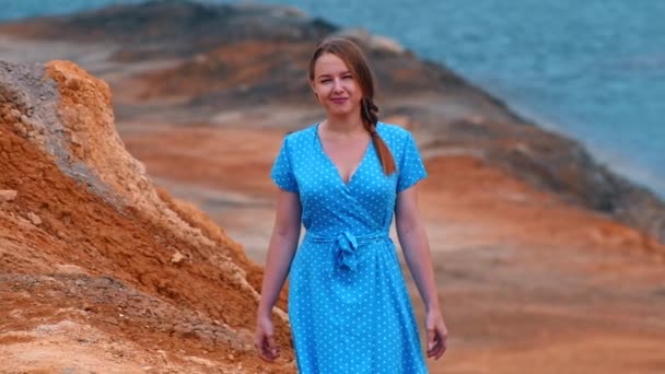 Młoda kobieta w niebieskiej sukience na tle pomarańczowej glinianej plaży i jeziora — Wideo stockowe