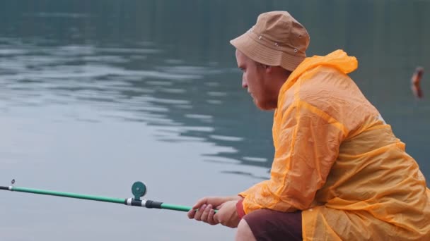 Hombre solitario sentado en una orilla y pescando — Vídeo de stock