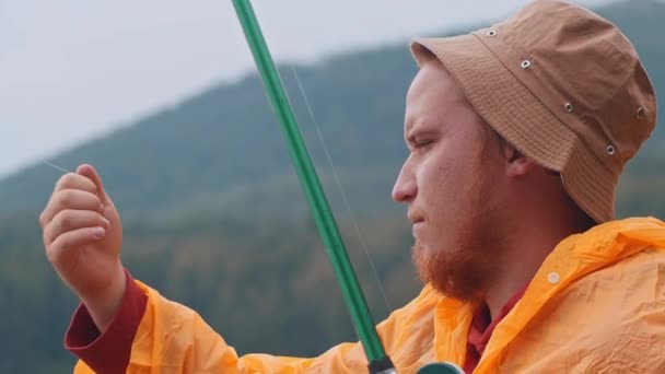 Ensam man sitter på en strand och fiskar - tittar på en krok med ett bete — Stockvideo
