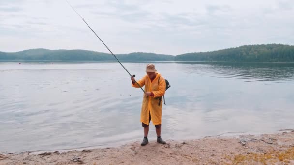 En man som håller i ett fiskespö och går iväg från stranden — Stockvideo