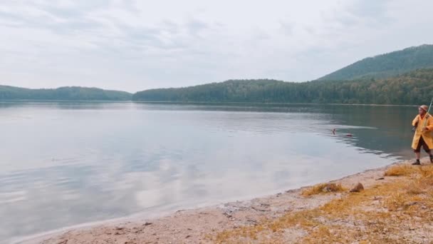 Un pescador camina a lo largo de la orilla - lago claro y dos botellas de plástico en el agua — Vídeos de Stock