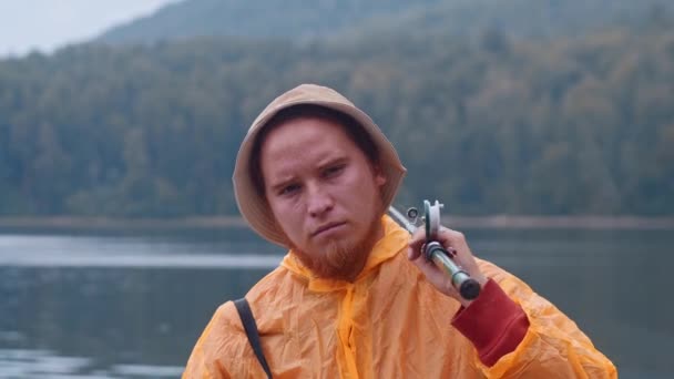 Triste pescador parado en una orilla sosteniendo su caña de pescar — Vídeo de stock