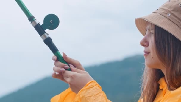 Γυναίκα στρίβοντας το πηνίο μιας ράβδου αλιείας και κοιτάζοντας το άγκιστρο — Αρχείο Βίντεο