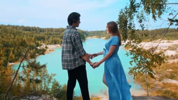 Young happy couple talking and holding hands on a background of blue lake and forest — Stock Video