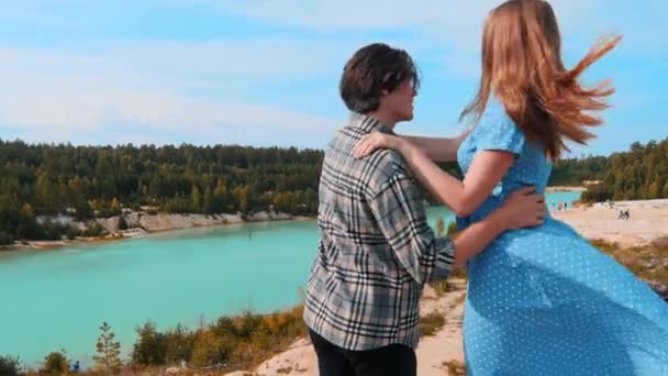 Молодая счастливая пара, стоящая на скале и смотрящая на голубое озеро и лес - наслаждаясь моментом — стоковое видео