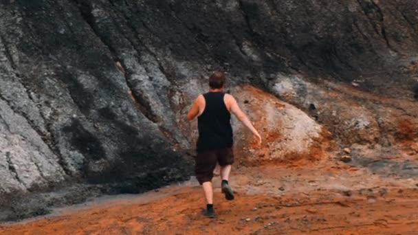 Um corredor homem em camisa preta correndo em uma montanha de barro laranja — Vídeo de Stock