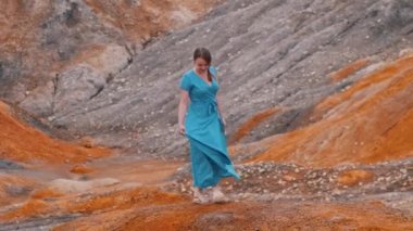 Mavi elbiseli genç kadın kil bir dağda dans ediyor.