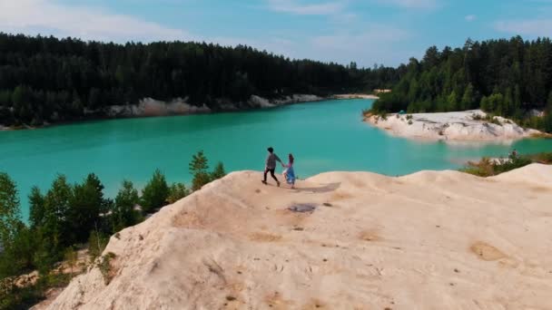 Um casal correndo em uma rocha perto do lago azul — Vídeo de Stock