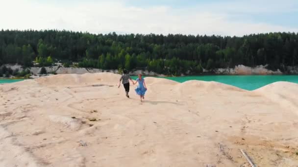 Happy couple holding hands and running to the cliff - a landscape of blue muddy lake and forest — Stock Video