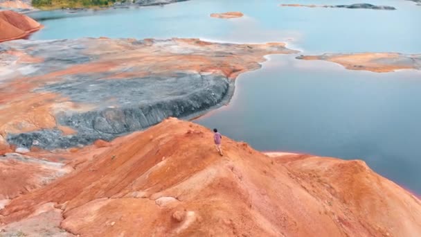 Muž běžící na hliněné hoře a zvedající ruce - krajina z červeného jezera a zeleného lesa — Stock video