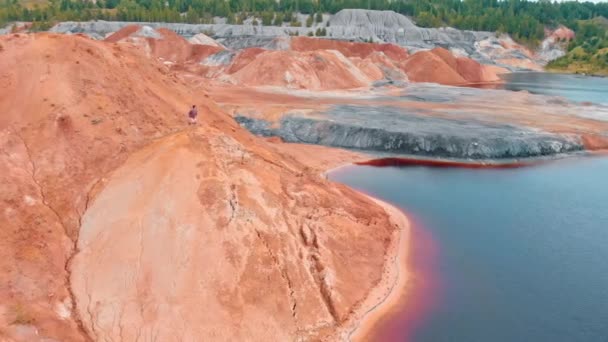 Человек бежит на глиняной горе и поднимает руки вверх - пейзаж красного озера и огромных глиняных гор — стоковое видео