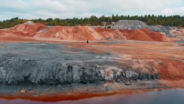 Un hombre corriendo sobre una montaña de barro - paisaje inusual de agua roja y montañas — Vídeo de stock