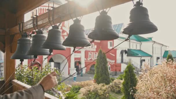 Osoba zvoní zvonky tahání za provazy v blízkosti červeného křesťanského kostela — Stock video