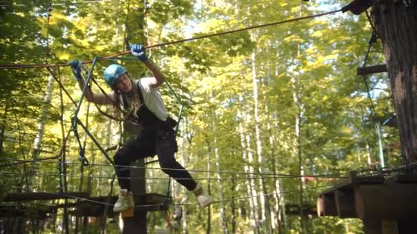 Une femme avec un casque et d'autres protections marche sur la corde entre les arbres une aventure extrême de corde — Video